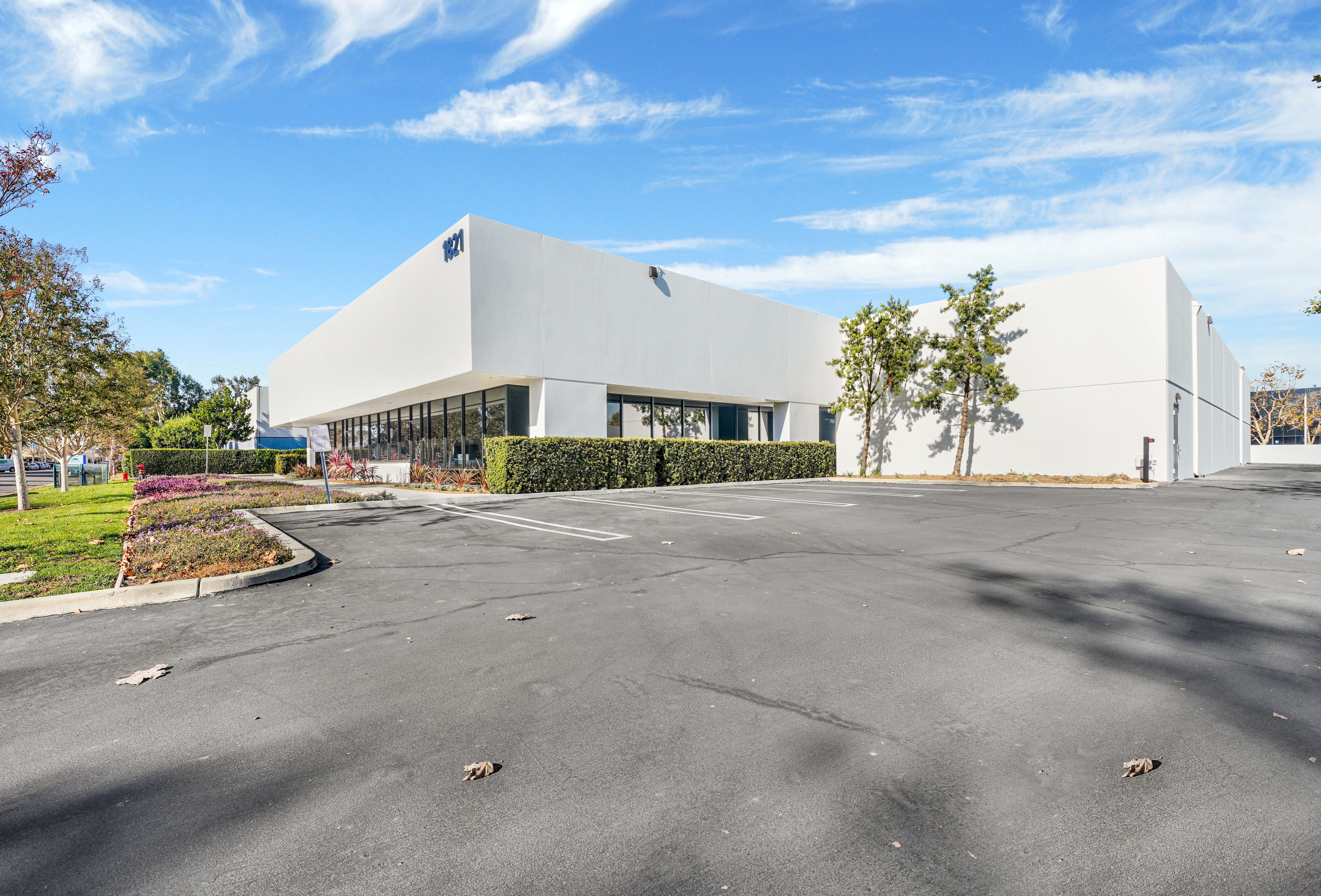 Exterior of a white industrial building at 1821 Kettering Street in Irvine, CA, featuring clean landscaping, ample parking, and a bright blue sky backdrop.